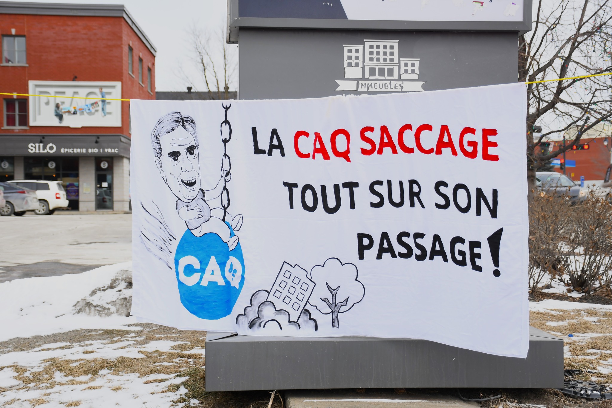 bannière contenant la phrase "La CAQ saccage tout sur son passage" avec une image de Legault sur un wrecking ball qui démolit des maisons et arbres